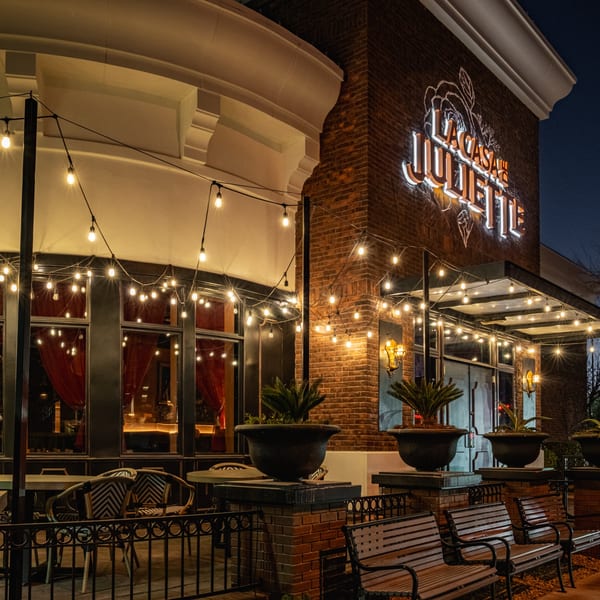 Exterior of La Casa de Juliette restaurant at night, with string lights, outdoor seating, and a glowing sign.