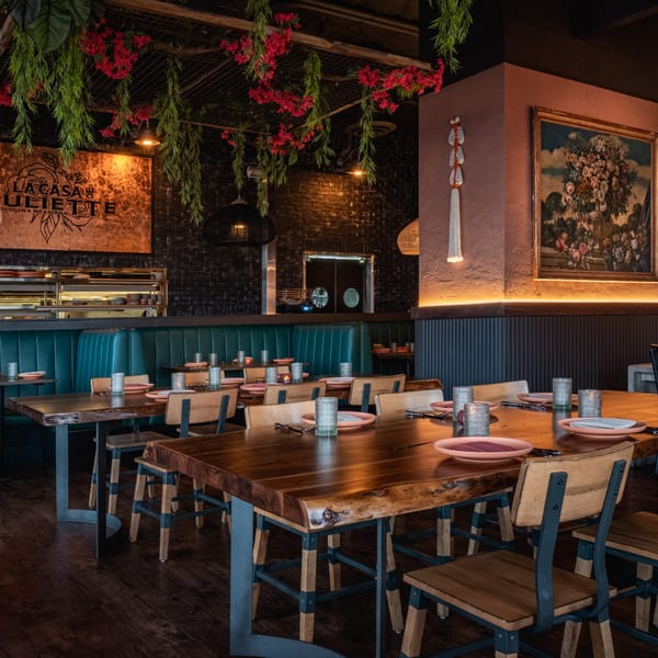 Interior of La Casa de Juliette restaurant with wooden tables, teal booths, and hanging red flowers.