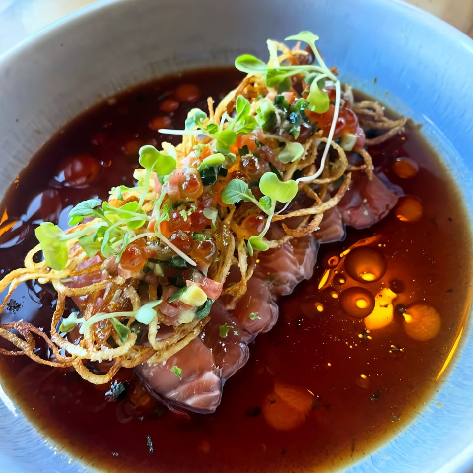 La Casa De Juliette's salmon dish with crispy onions, microgreens, and roe in a dark sauce.