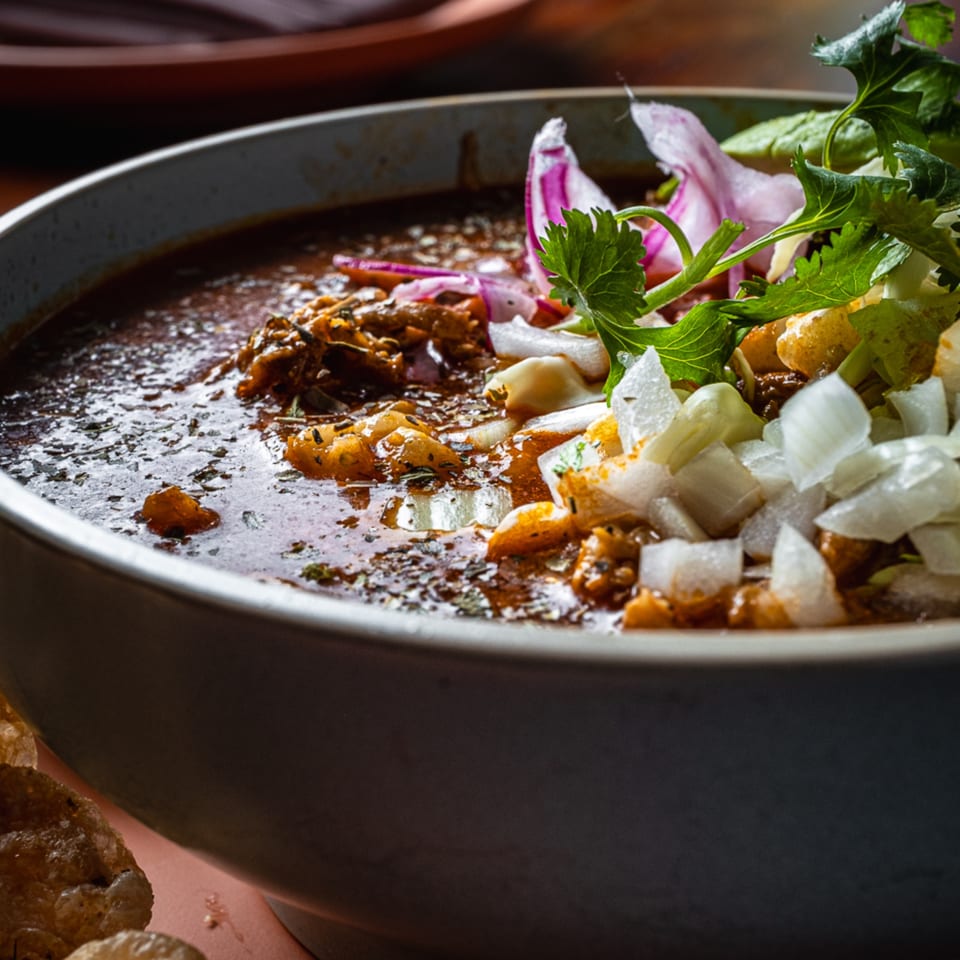 Close-up of a Mexican stew, garnished with diced onions, red onions, and fresh cilantro.