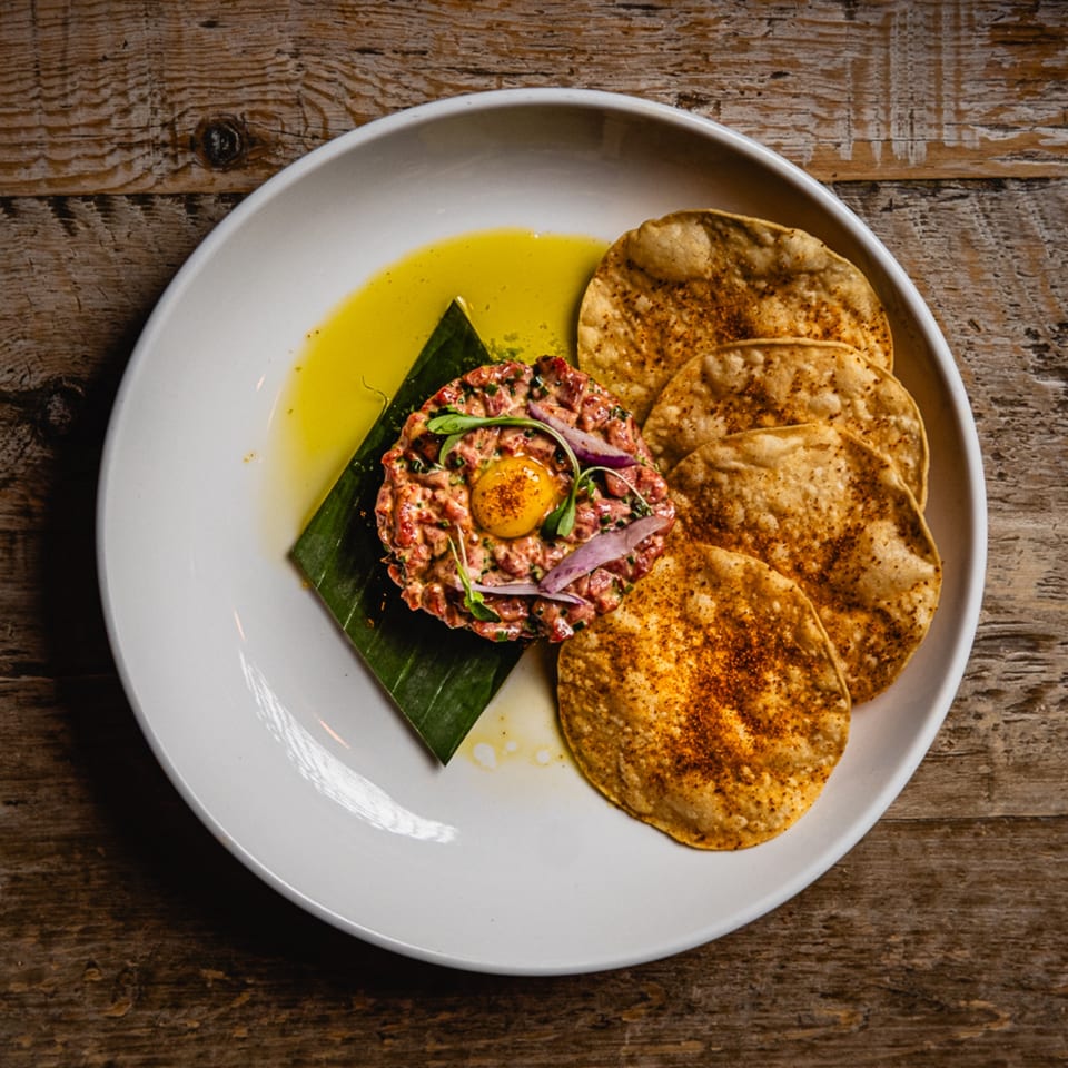Mexican beef tartare with a raw egg yolk, red onions, and crispy tortillas on a white plate.